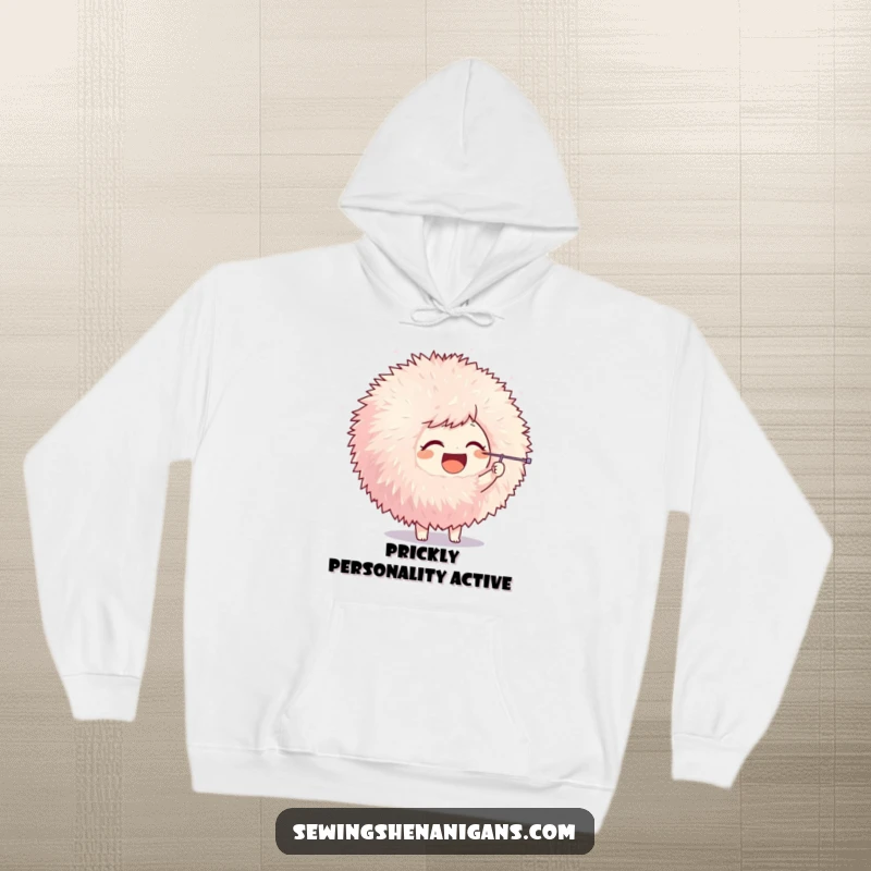 Funny hoodie featuring a joyful character playfully poking a large pom-pom with a needle, offering warmth and crafting amusement.
